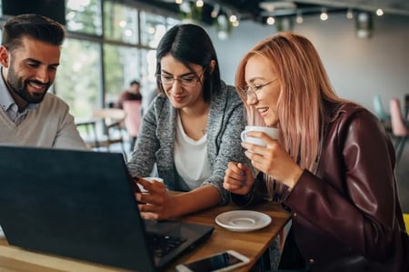 Three happy people discussing something on a laptop at a coffee shop